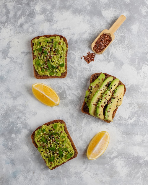 Avocado open toast with avocado slices, lemon, flax seeds, sesame seeds, black bread slices, top view