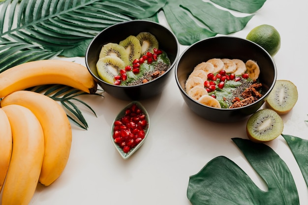 Free photo avocado smoothie bowl topped with chia, granola, kiwi and  spinach.  overhead, top view, flat lay. healthy breakfast. tropical  leaves.