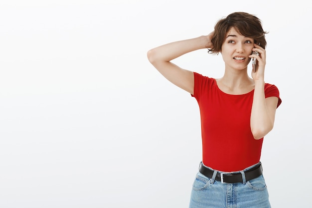 Awkward and indecisive cute woman scratching head clueless while talking on phone