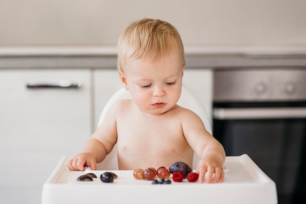 Baby boy in highchair choosing what fruit to eat