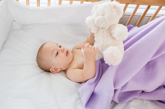 Baby boy playing with a soft toy on a cradle