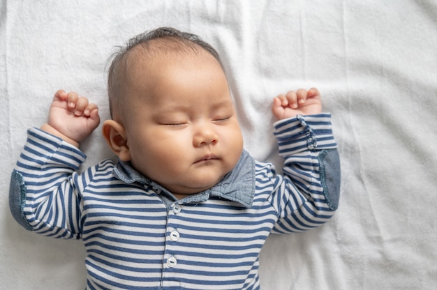 A baby boy in a striped shirt is sleeping in bed.