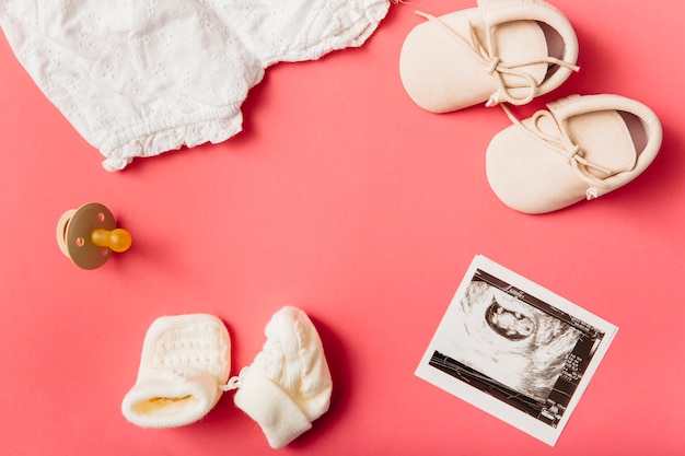 Free photo baby clothing; socks; pacifier; pair of shoes and ultrasound picture on peach background