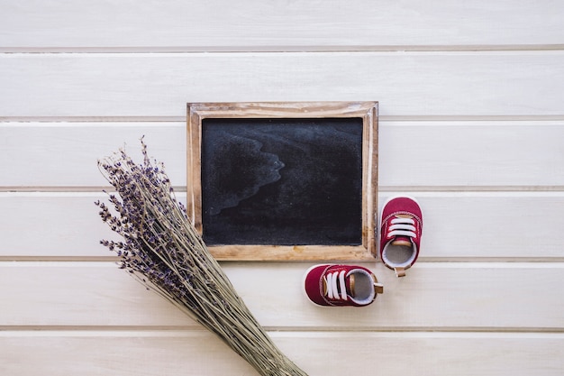 Baby concept with slate, branches and shoes on wooden surface