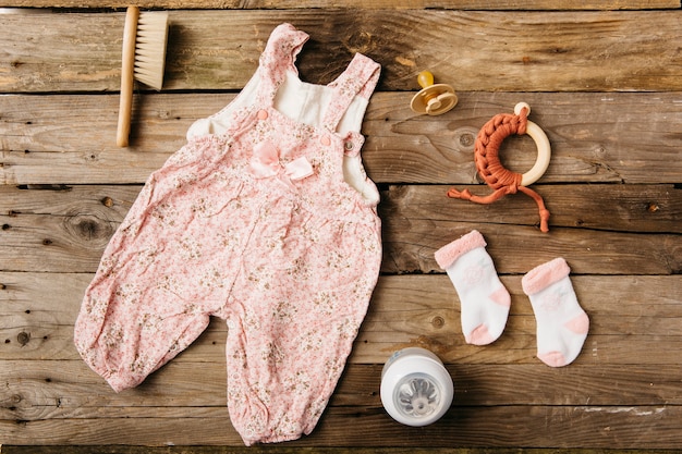 Free photo baby's dress; brush; pacifier; toy and pair of socks with milk bottle on wooden table