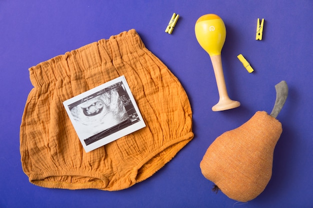 Free photo baby's short; stuffed pear; rattle and yellow clothespin on blue background