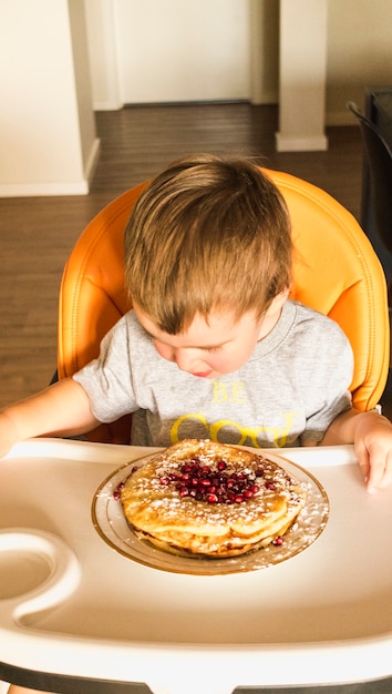 Baby sitting on high chair looking at pancake on plate