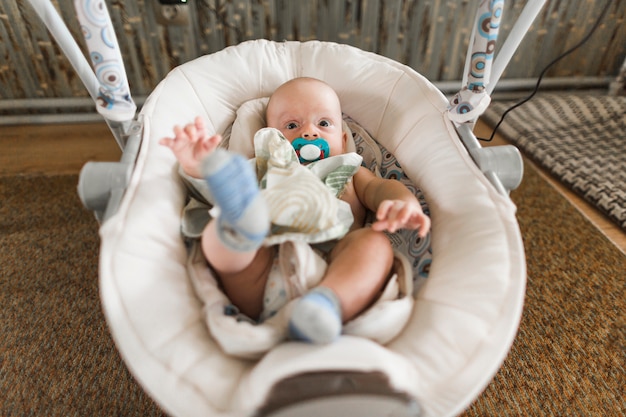 Free photo baby with pacifier lying on baby carriage at home