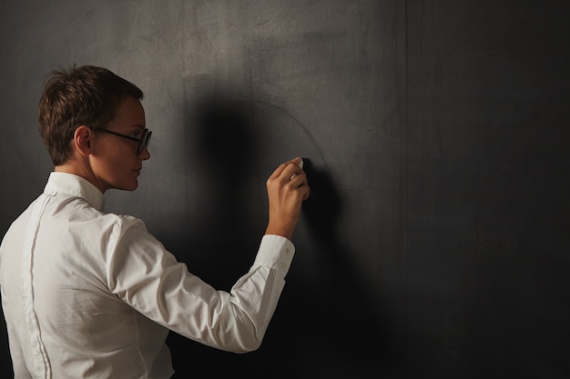 Free Photo back portrait of a serious female teacher in a white shirt starting to write onn empty blackboard