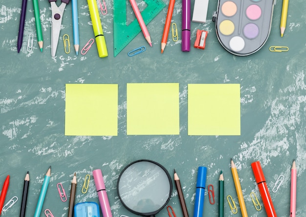 Back to school concept with sticky notes, magnifying glass, school supplies on plaster background flat lay.