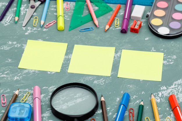 Back to school concept with sticky notes, magnifying glass, school supplies on plaster background high angle view.