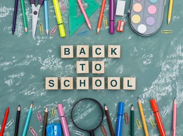 Free photo back to school concept with wooden cubes, magnifying glass, school supplies on plaster background flat lay.