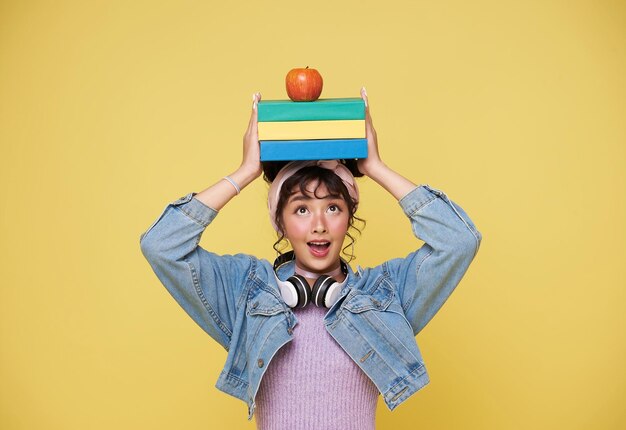 Free photo back to school happy smiling young asian college student with book and red apple on head