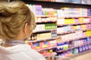 Free photo back shot of grandmother with blonde hair shopping at local supermarket, pushing cart forward going to household chemistry