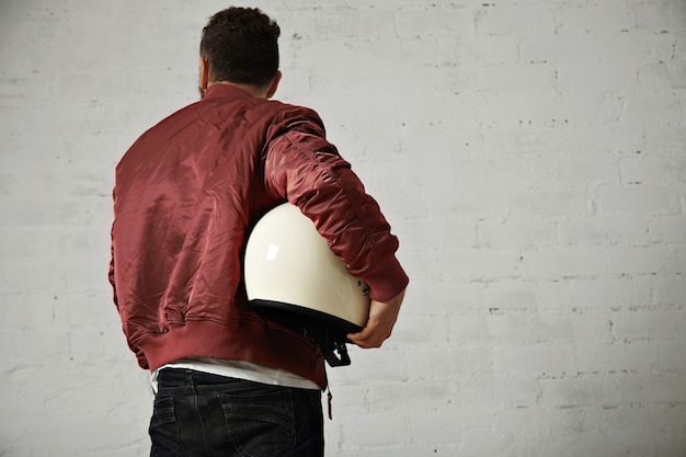 Free photo back shot of a man in jeans, short terracotta jacket with a sparkling white motorcycle helmet under his arm isolated on white