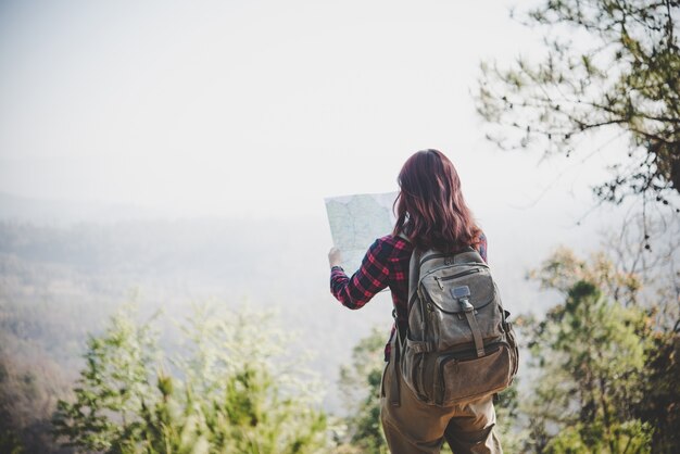 Back side of traveler girl searching right direction on map, while traveling to hiking in the mountain. Travel concept.