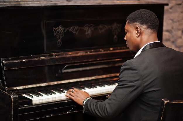 Free photo back of strong powerful african american man in black suit play piano