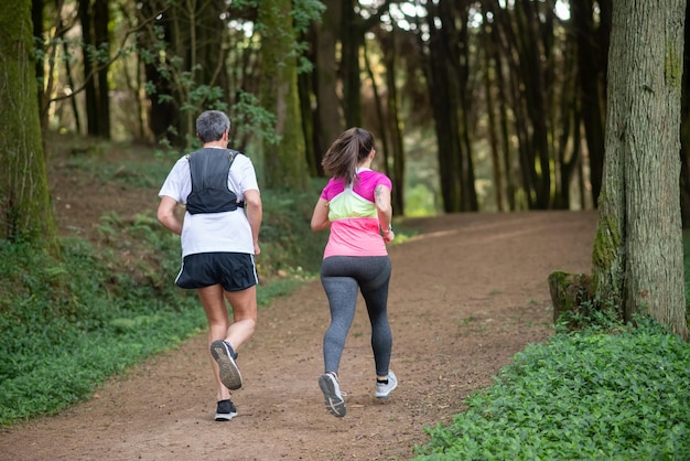 Free photo back view of active man and woman jogging in forest. two sporty people in sportive clothes exercising outdoors. sport, hobby concept