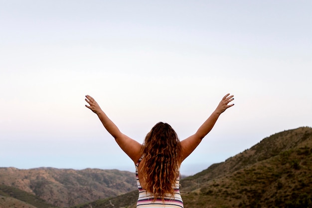 Back view of carefree woman outdoors with hands up