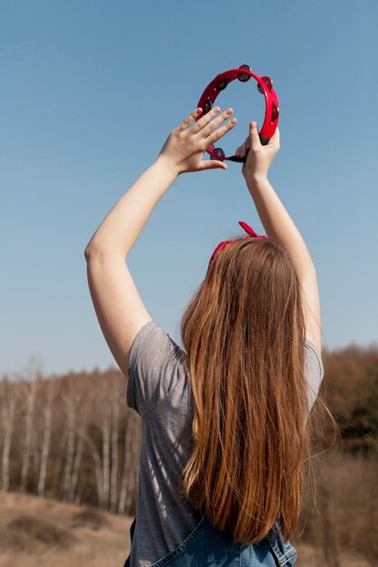 Back view of of carefree woman playing the tambourine in nature