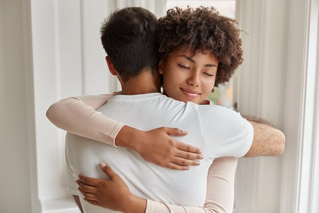 Back view of Caucasian guy embraces her girlfriend, stand closely to each other, express love and support, comfort, express empathy, have good relations. People, care and relationship concept