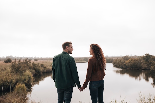 Back view couple holding hands next to a pond