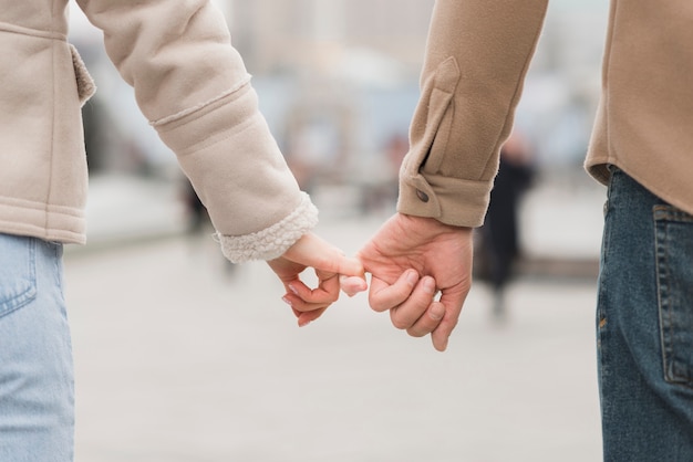 Back view of couple holding pinkies outside