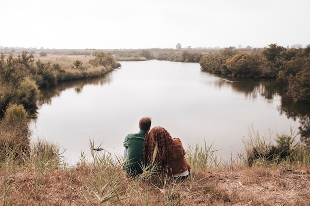 Back view couple sitting next to a pond