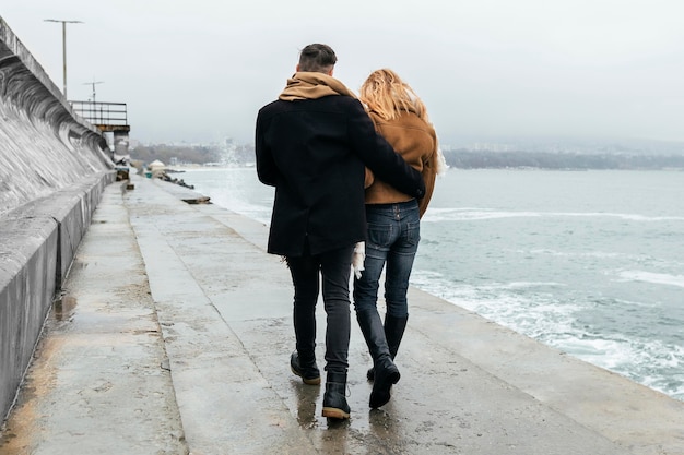 Back view of couple walking embraced by the beach in winter