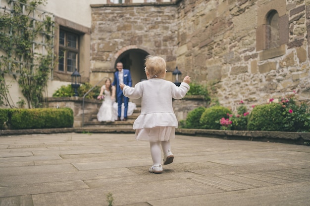 Back view of a cute baby girl runs toward parents