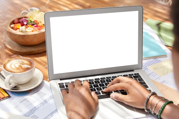 Free photo back view of dark skinned woman sits in front of opened laptop computer with blank empty white screen for your advertisement