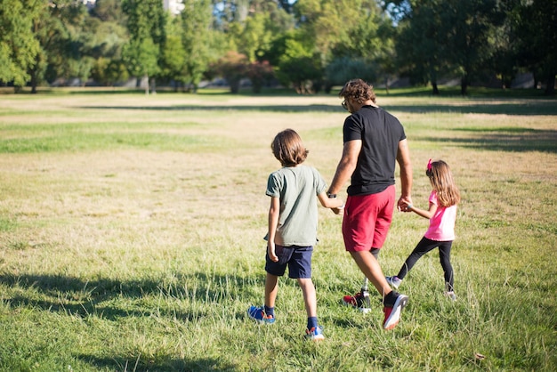 Back view of father with disability walking with children. Man with mechanical leg having walk in park with boy and girl. Disability, family, love concept