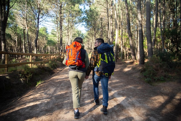 Free Photo back view of fond couple of young hikers. caucasian man with beard and woman with dark hair with big backpacks holding hands. hobby, nature, love concept