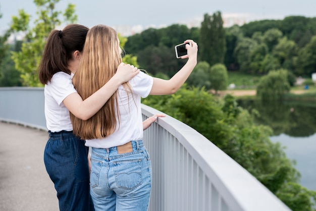 Free photo back view girls taking a selfie on a bridge