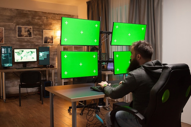 Back view of hackers in front of computer with multiple screens with green mock up.