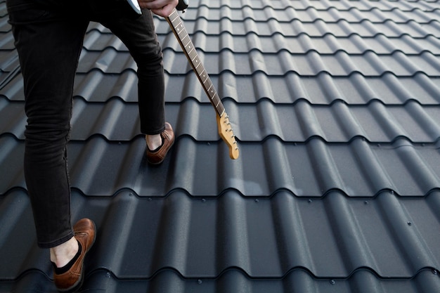 Back view of male musician climbing roof with electric guitar