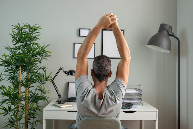 Free photo back view of man at desk stretching while working from home