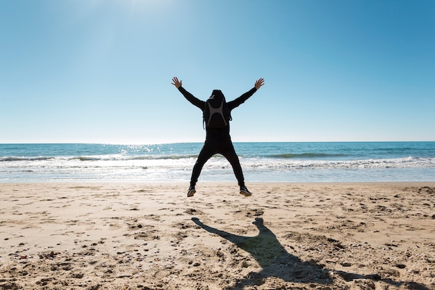 Free photo back view man jumping near sea