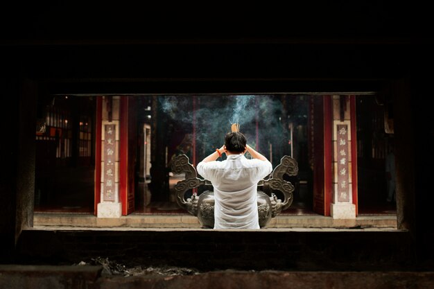 Back view of man praying at the temple with burning incense