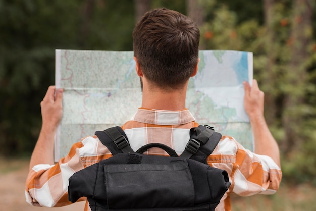 Back view of man with backpack looking at map while camping