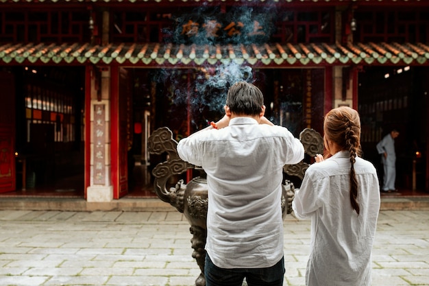 Back view of man and woman praying at the temple with burning incense