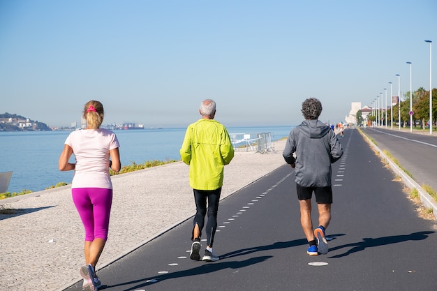 Back view of mature people wearing sports clothes, jogging along river bank. Full length. Retirement or active lifestyle concept