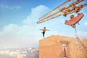 Free photo back view of muscular and athletic man doing exercise on high brick wall. un finishing building on high. big iron crane and cityscape on background.