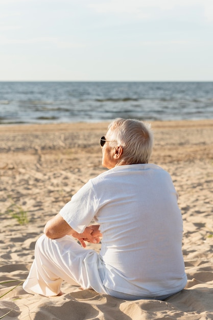 Back view of older man admiring the view at the beach while resting in the sun