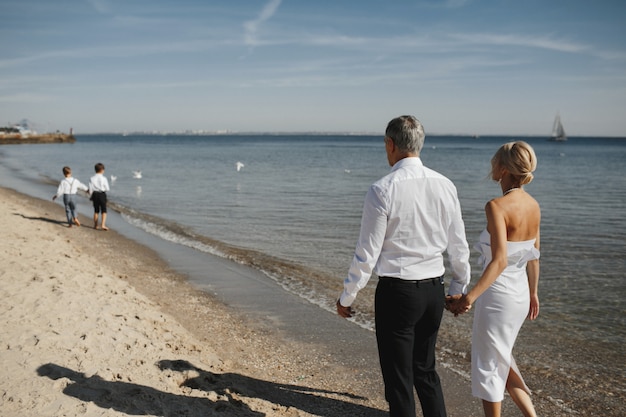 Free photo back view of parents, who are holding hands together and two young sons in front of them on the coastline