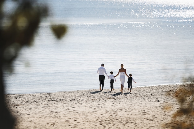 Back view of running family on the beach on the sunny day near the sea dressed in fashionable clothes