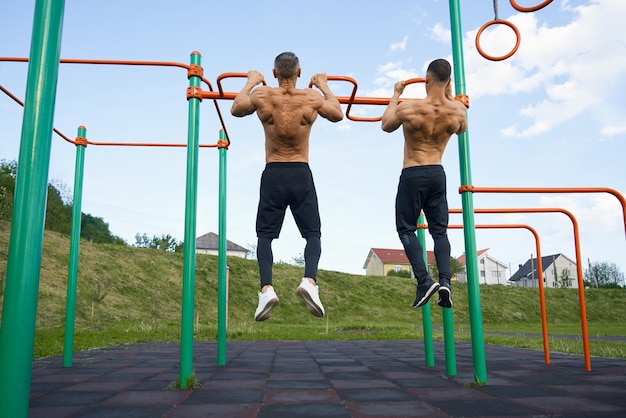 Back view of shirtless bodybuilders doing pull ups outdoors