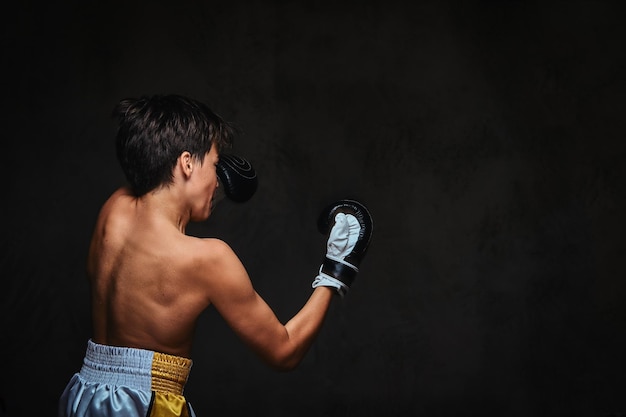 Back view of a shirtless young boxer during boxing exercises, focused on process with serious concentrated facial.