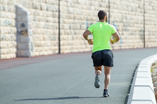 Back View of Strong Sporty Man Running on Road