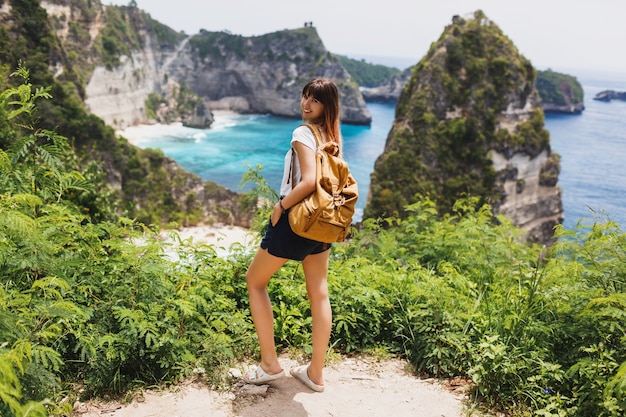 Back view of traveling woman standing on cliffs and tropical beach